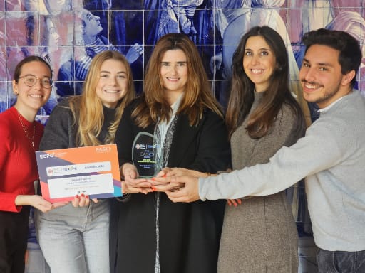 Five people smiling, holding an award and a certificate in front of a blue patterned background.